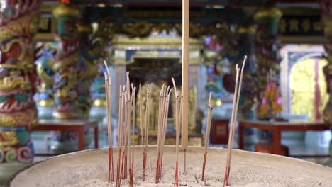 Close-up-group-of-joss-sticks-in-a-big-pot,-with-blurred-background-of-a-Chinese-temple-or-shrine