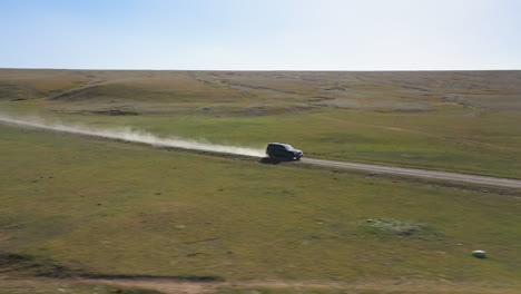 Epic-cinematic-drone-shot-of-the-dust-kicking-up-behind-an-SUV-along-the-road-near-the-Kel-Suu-lake-in-Kyrgyzstan