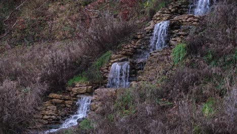 Small,-idyllic-cascading-waterfall-stream-surrounded-by-Wintery-brown-garden-landscape-in-rural-English-countryside-garden-park
