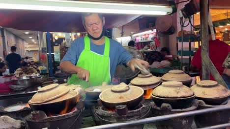 Street-Food-Stall,-Malaysischer-Mann,-Der-Nachts-Auf-Tontöpfen-In-Der-Straße-Von-Kuala-Lumpur-Kocht