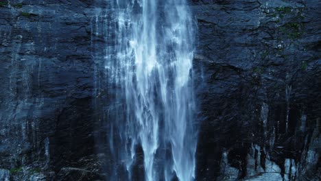 Ascending-shot-of-smooth-waterfall-crashing-down-rocky-mountain-wall-in-Norway