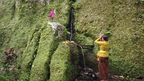 Balinese-Woman-Praying-under-The-Water-in-Stone-Moss-Temple-Goa-Garba,-Melukat-Ritual-of-Bali-Hinduism,-Holding-Hands-Together-for-the-Gods,-Peaceful-and-Meditative