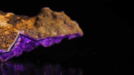 Smooth-captivating-pan-of-a-purple-amethyst-crystal-lit-against-a-black-background