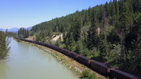 Die-Antenne-Folgt-Dem-Zug,-Der-Kohle-Neben-Dem-Bow-River-In-Den-Kanadischen-Rocky-Mountains-Transportiert