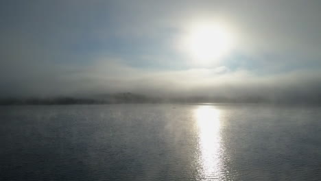 Beautiful-sunrise-aerial-over-foggy-lake-with-sun-beam-and-one-boat