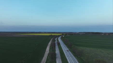 Aerial-cinematic-view-of-cars-driving-between-the-trees-and-fields-on-countryside-roadway-with-rural-roads-on-the-side