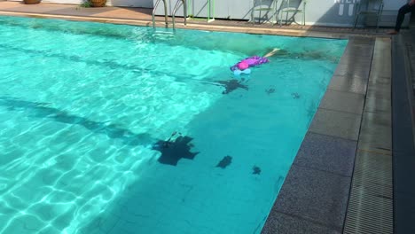 Asian-small-child-girl-practices-swimming-in-the-pool,-outdoor-swimming-pool