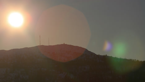 Tele-shot-of-sun-going-down-along-a-mountain-ridge-with-a-beautiful-lens-flare-before-disappearing
