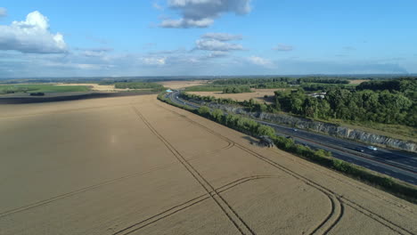 Establishing-Drone-Shot-of-Combine-Harvester-Harvesting-on-Sunny-Day-next-to-Motorway-with-Traffic
