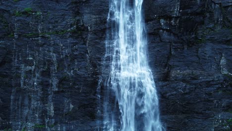 Tilt-up-shot-showing-waterfall-falling-in-front-of-steep-mountain-wall-during-dusk---Slow-motion-shot