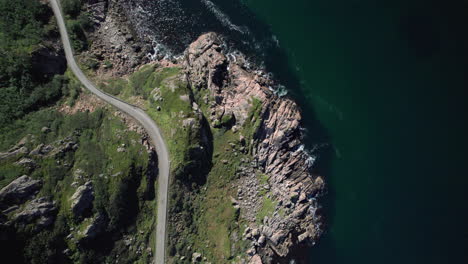 Aerial-top-down-shot-of-a-narrow-dangerous-Norwegian-road-along-the-coastline-on-a-sunny-day