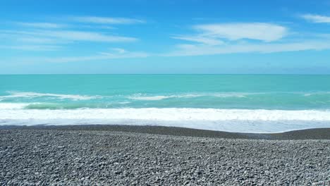 Low-aerial-slow-motion-of-small-waves-breaking-onto-stony-beach-at-Canterbury-Bight---beautiful-turquoise-colored-South-Pacific-Ocean