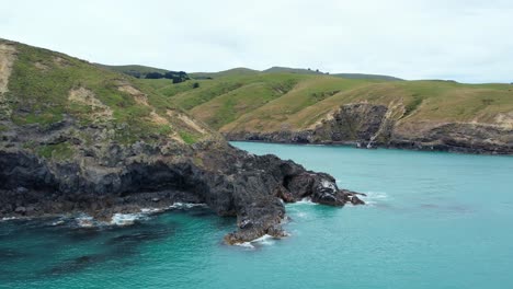 Aerial-descent-above-beautiful-turquoise-colored-South-Pacific-Ocean-towards-diverse-volcanic-rock-formations-at-Banks-Peninsula