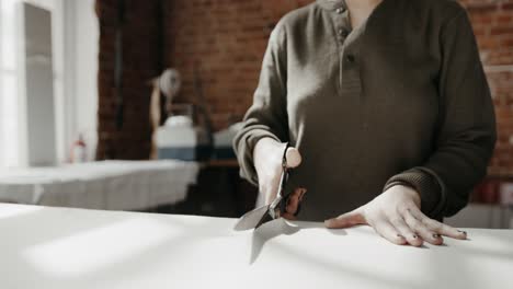 Front-view-of-a-female-tailor-cutting-clothing-fabric-with-scissors,-fashion-designer-working-studio