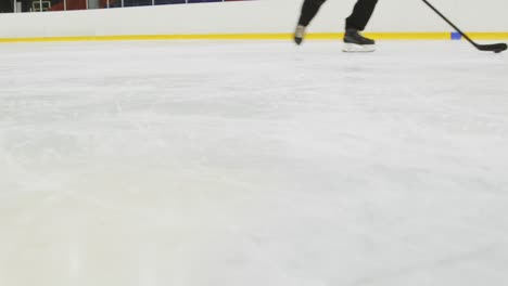 Hockey-players-training-on-the-ice-rink-with-hockey-sticks-and-pucks,-low-angle-shot-of-hockey-skates