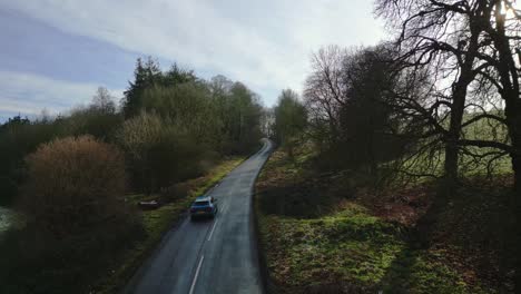 Aerial-drone-shot-of-a-car-in-an-uk-country-road-in-the-winter-at-sunset