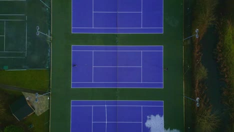 Top-down-drone-shot-of-people-playing-in-a-blue-tennis-court