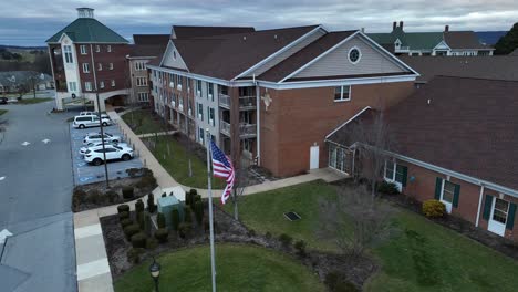 Aerial-rising-shot-of-American-flag-waving-in-front-of-brick-retirement-home-building
