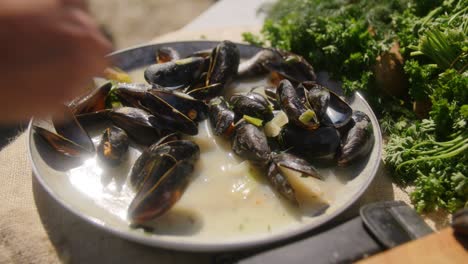 A-plate-of-fresh-mussels-on-a-sunny-day-in-the-summer-while-a-person-grabs-one-mussel-to-eat