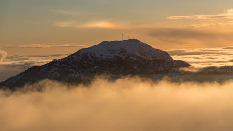 Inversion-clouds-surrounding-snow-capped-mountain-Løvstakken-in-Bergen,-Norway