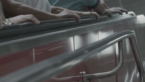 A-medium-shot-of-multiple-people-going-up-an-escalator,-captured-with-a-static-camera,-showing-only-arms-and-hands-in-focus