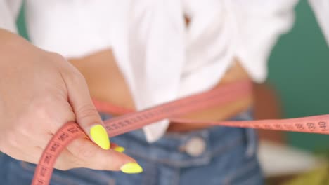 Close-up-of-woman-while-happily-measuring-her-waist,-using-clothing-measuring-tape,-weight-loss-concept