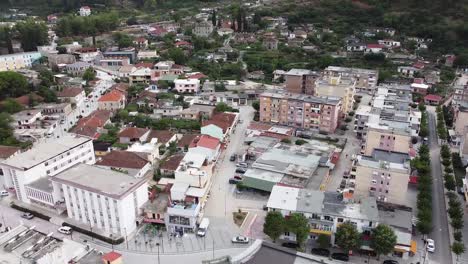 Panoramic-aerial-view-of-a-village-next-to-a-river,-with-cars-driving-on-the-streets,-Albania