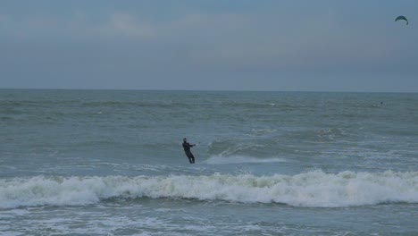 Man-engaged-in-kitesurfing,-overcast-winter-day,-high-waves,-Baltic-Sea-Karosta-beach-,-slow-motion,-medium-shot