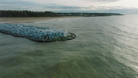 Aerial-establishing-view-of-protective-pier-with-concrete-blocks-and-rocks-at-Baltic-sea-coastline-at-Liepaja,-Latvia,-strengthening-beach-against-coastal-erosion,-ascending-drone-shot-moving-forward