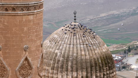 Mardin-Ulu-Camii's-minaret-and-dome-in-the-same-frame,-camera-is-zooming-in-to-the-dome-where-you-can-see-the-pigeons-settling-on-the-dome-on-a-cloudy-day