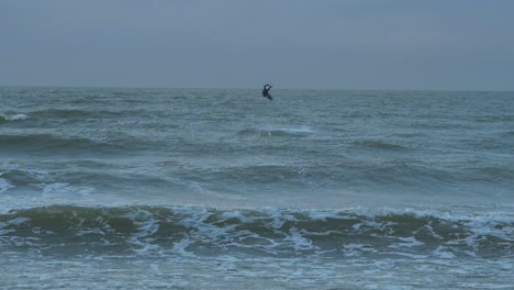 Man-engaged-in-kitesurfing,-overcast-winter-day,-high-waves,-Baltic-Sea-Karosta-beach-,-slow-motion-jump,-wide-distant-shot