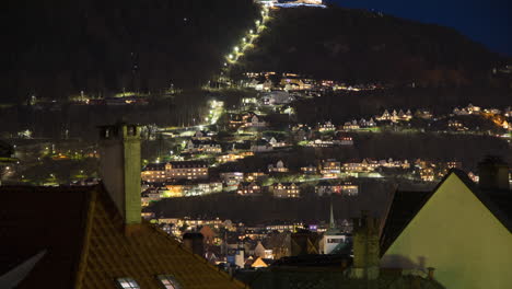 Beautiful-view-of-Fløybanen-funicular-in-Bergen-at-night,-with-people-wearing-headlamps-walking-up-and-down-the-curved-roads-to-the-summit