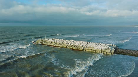 Aerial-establishing-view-of-protective-stone-pier-with-concrete-blocks-and-rocks-at-Baltic-sea-coastline-at-Liepaja,-Latvia,-strengthening-beach-against-coastal-erosion,-ascending-drone-shot-tilt-down