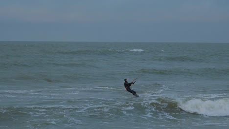 Active-man-engaged-in-kitesurfing,-overcast-winter-day,-high-waves,-Baltic-Sea-Karosta-beach-,-slow-motion,-distant-medium-shot