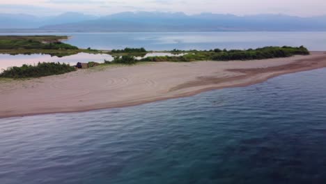 The-drone-flew-away-over-a-lake,-revealing-wild-campers-camping-on-a-wild-beach-island-with-a-sunset-and-a-big-lake-in-the-background