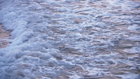 Unsettling-sea-water-reflects-pink-sunlight-as-foamy-wave-washes-over