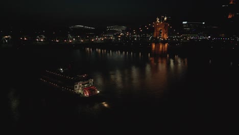 Aerial-Night-Pan-of-Paddle-Steamer-and-Suspension-Bridge-in-Ohio-River,-Cincinnati,-Ohio