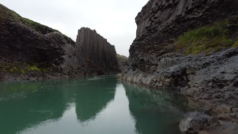 A-blue-river-in-Studlagil-Canyon,-Iceland-with-basalt-rock-columns,-front-view,-moving-in