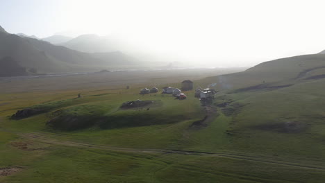 Toma-Aérea-Cinematográfica-Giratoria-De-Un-Campamento-De-Yurtas-Cerca-Del-Río-Kurumduk-En-Kirguistán,-Hacia-El-Sol