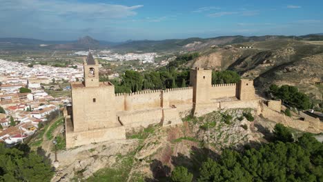 Antequera-Fortress-and-waving-Spanish-flag-in-Andalusia,-Spain---Aerial-4k-Circle-Shot