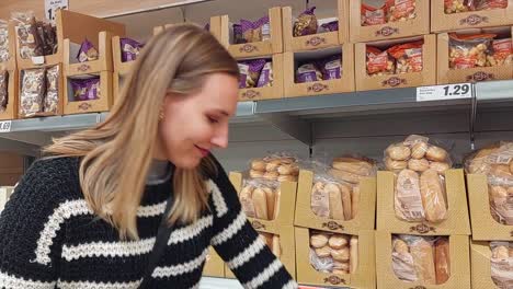 Young-blonde-woman-picking-and-selecting-a-bag-of-bread-from-a-supermarket