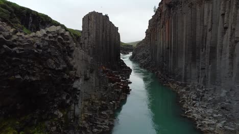 Studlagil-Canyon,-wide-pushing-in,-blue-river-in-Iceland-with-basalt-rock-columns,-front-view