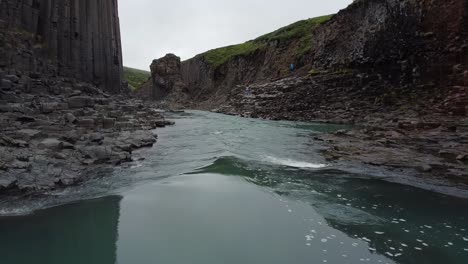 A-blue-green-river-in-Studlagil-Canyon,-Iceland-with-basalt-rock-columns,-reverse-view,-moving-in