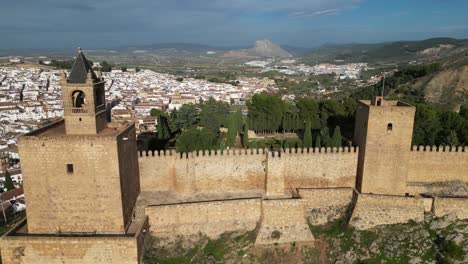 Antequera-Fortress-and-Spanish-waving-flag-in-Andalusia,-Spain---Aerial-4k-Circle-Shot