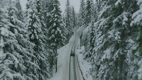 An-electric-vehicle-driving-on-a-narrow-road-in-a-beautiful-snowy-landscape-in-Norway-with-snow-covered-tree-tops