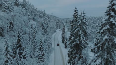 Drohnenaufnahmen-Eines-Elektroautos,-Das-In-Einer-Wunderschönen-Verschneiten-Landschaft-In-Norwegen-Mit-Schneebedeckten-Baumkronen-Fährt