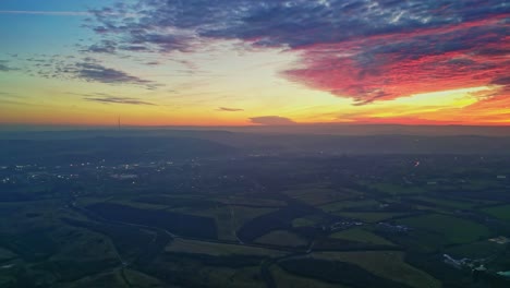 Drone-Cinematic-Countryside-Scenery-Green-Misty-Fields-Colorful-Red-Sunset-Horizon-Fiery-Clouds