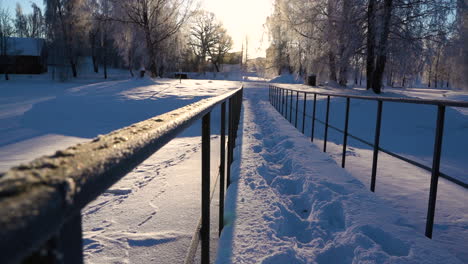 Small-foot-bridge-covered-in-deep-snow-layer-with-person-walk-marks-on-sunny-winter-day