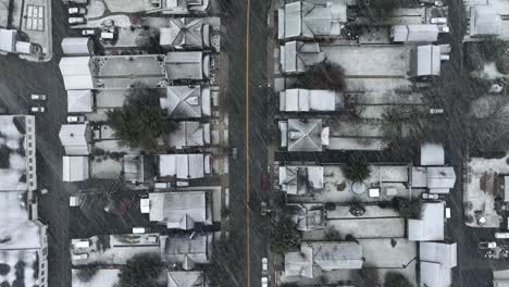 Top-down-aerial-view-of-white-roofs-of-houses-and-homes-in-small-town-America-during-beautiful-heavy-snowstorm-in-dead-of-winter