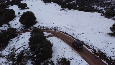 4x4-vehicle-truck-car-on-dirt-road-mountain-covered-with-white-snow,-aerial